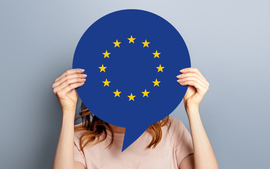 woman holds blank white speech bubble with european union flag isolated over grey studio background. News information channel concept